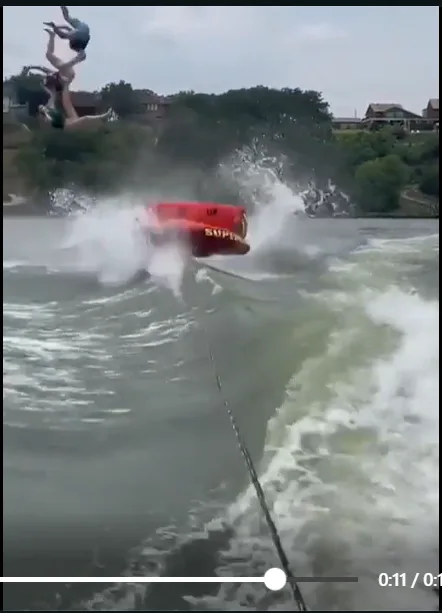A red boat labeled 'SUPER' is speeding across water, creating a large wake and splash, while two people are airborne above…