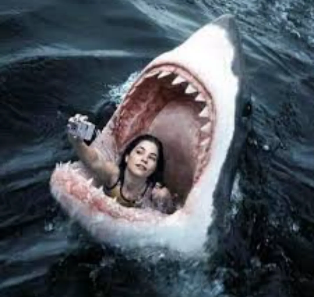 A woman is inside the open mouth of a large shark, holding up a phone as if taking a selfie, while looking calmly at the…