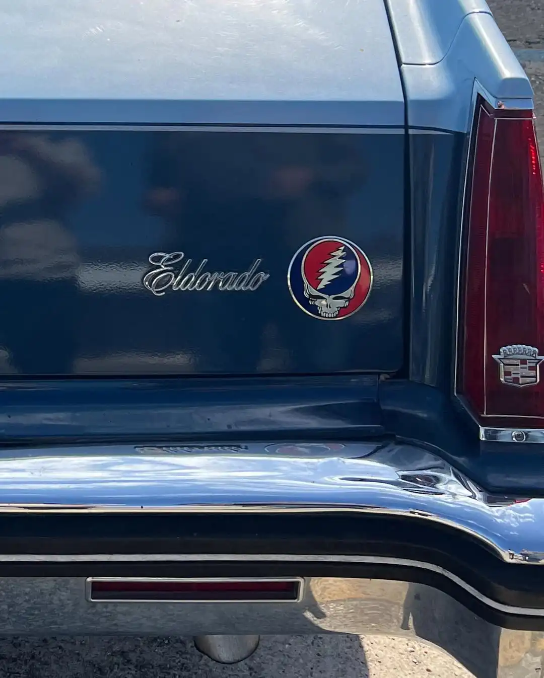 The rear of a blue Cadillac Eldorado features a chrome 'Eldorado' script emblem and a circular Grateful Dead 'Steal Your…