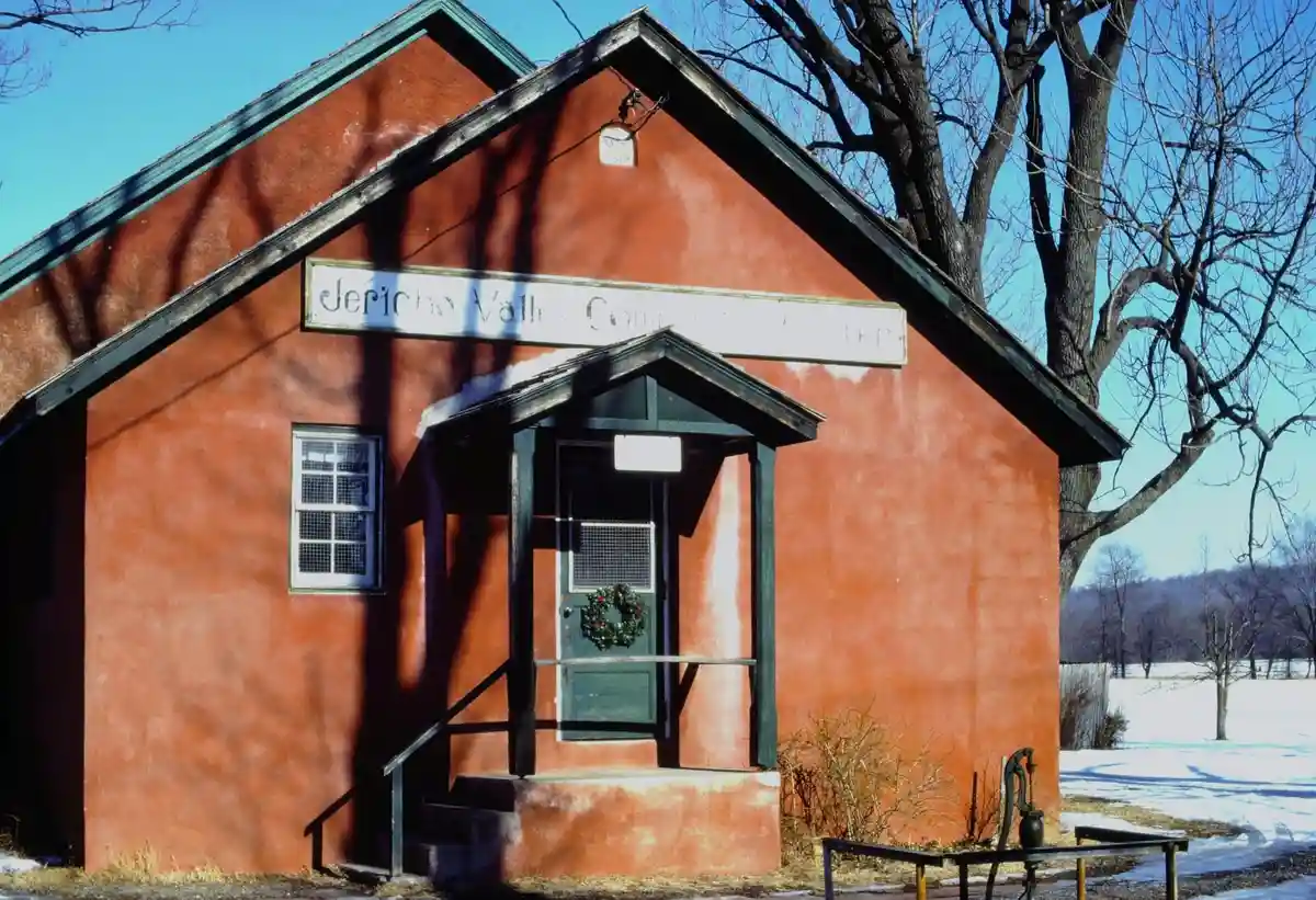 A red-painted building with a green-trimmed roof and door, labeled 'Jericho Valley Computer Center,' stands in a snowy…