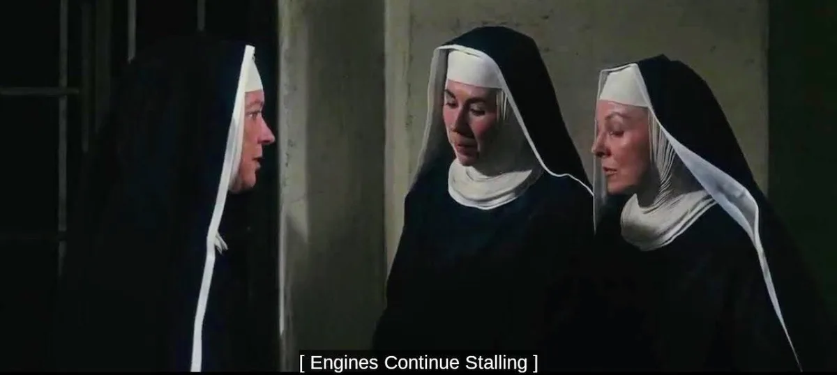 Three nuns in black habits with white veils stand in a dimly lit room, looking concerned. The nun on the left speaks while…