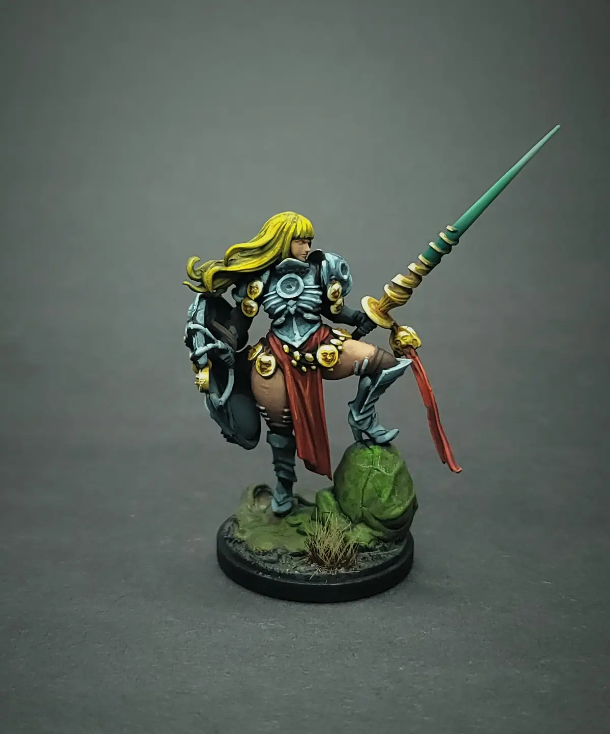 A painted miniature of a fantasy warrior with long blonde hair, wearing ornate silver armor with gold accents and a red…