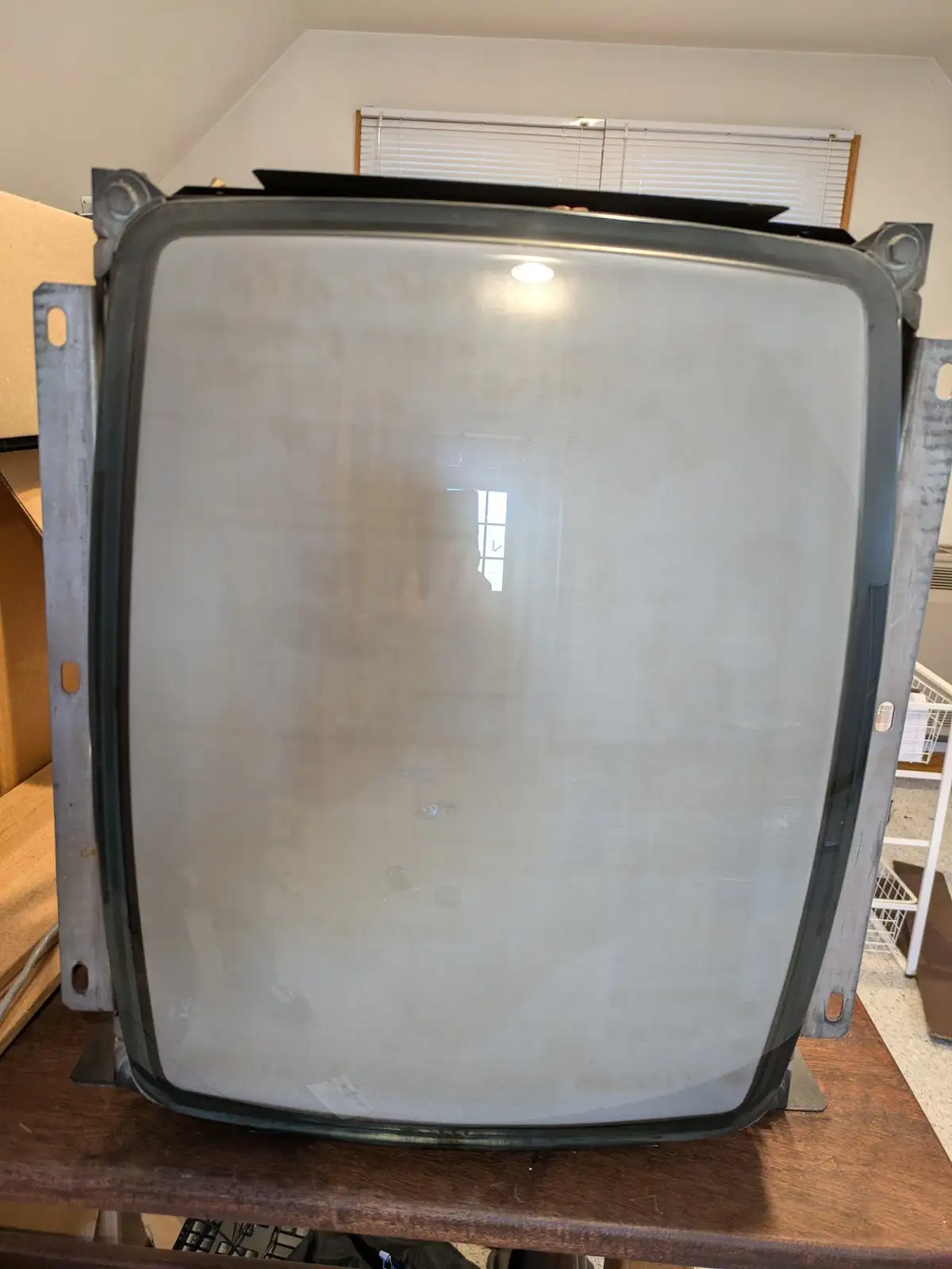 A large, old-style television screen with a thick metal frame sits on a wooden table, its glass surface completely fogged or…