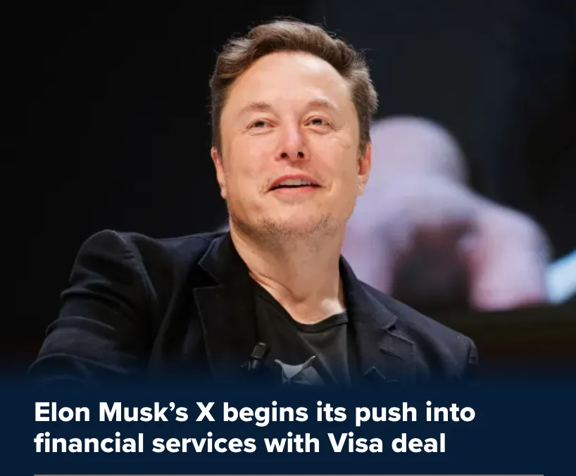 A close-up photo of Elon Musk smiling slightly while wearing a black blazer over a black t-shirt. A dark blue banner at the…