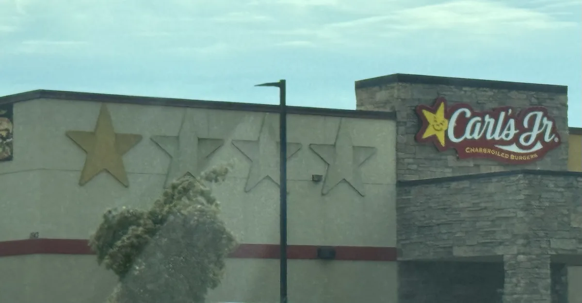 An exterior shot of a Carl's Jr. restaurant with its iconic yellow star logo and red signage. The building facade features…