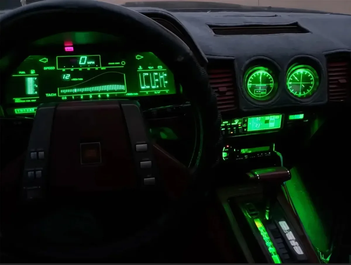 The image shows a car's dashboard at night, illuminated with bright green digital and analog gauges. The speedometer reads 0…