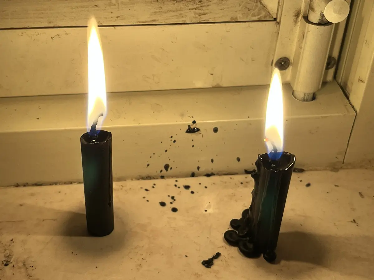 Two black candles burn on a white surface, one tall and straight, the other melted and dripping wax. The text overlaid says…