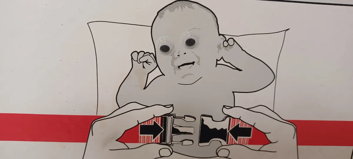 A printed diagram of a person in bed holding a seatbelt buckle, with googly eyes glued to the face, showing a frustrated…