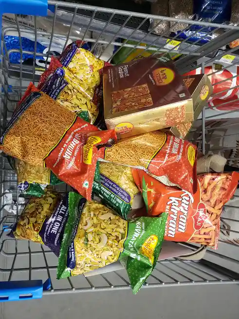 A shopping cart is overflowing with various Indian snack packages, including Bhujia, Peanut Gachak, and Navratan Makhana…