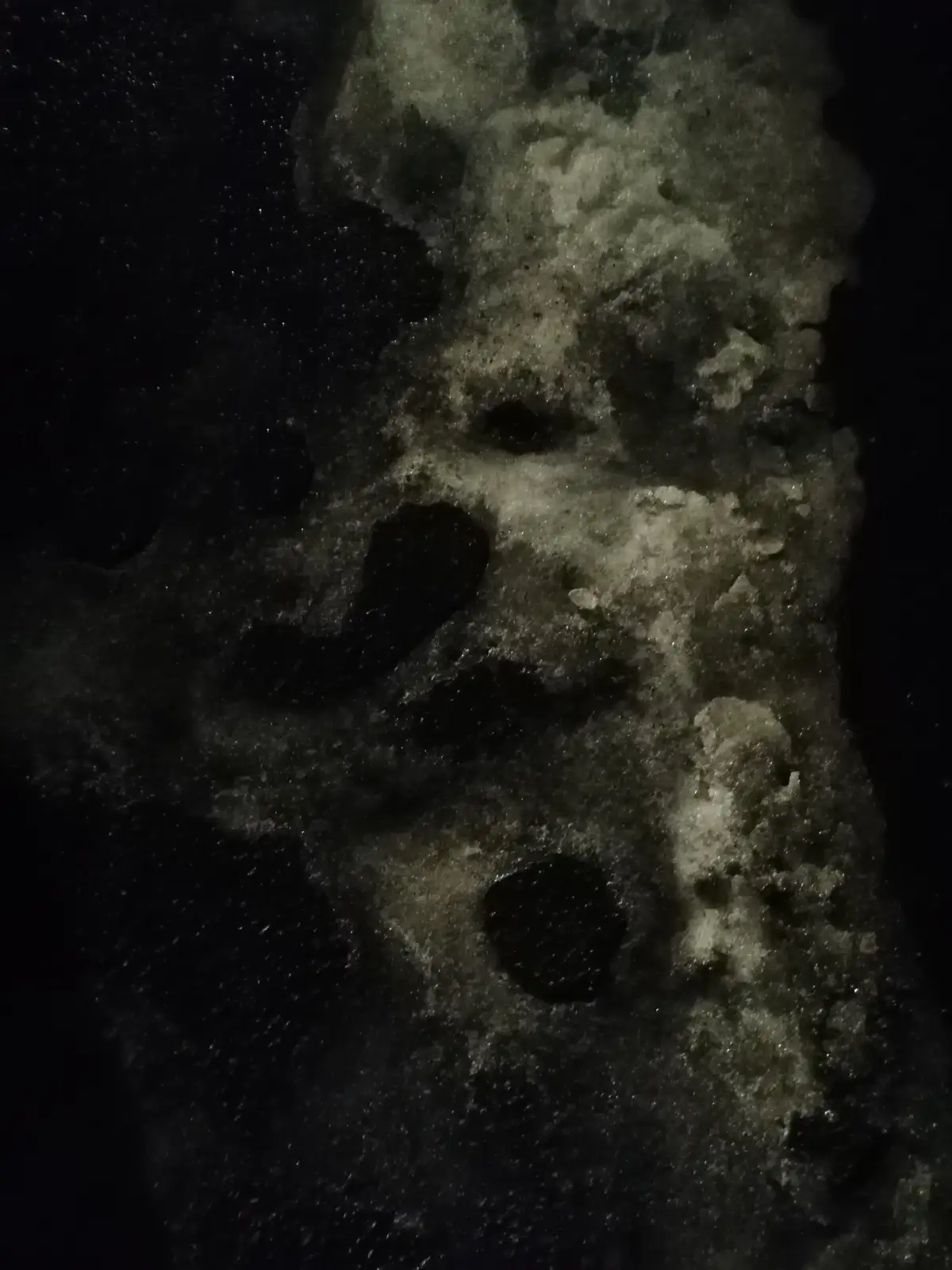 A close-up photo of a dark, textured surface with irregular light and dark patches that vaguely resemble a human face…