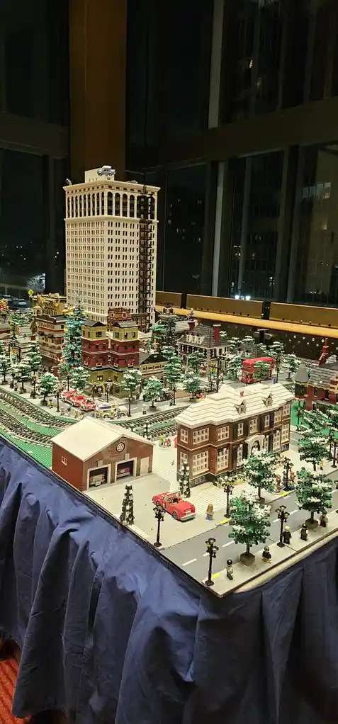 A detailed LEGO cityscape diorama featuring miniature buildings, streets, trees, and vehicles, all constructed from LEGO…