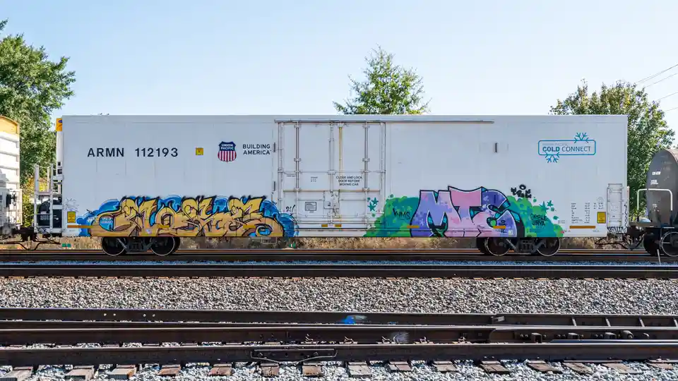 A white Union Pacific refrigerated railcar, marked with 'ARMN 112193' and 'BUILDING AMERICA', sits on tracks with vibrant…