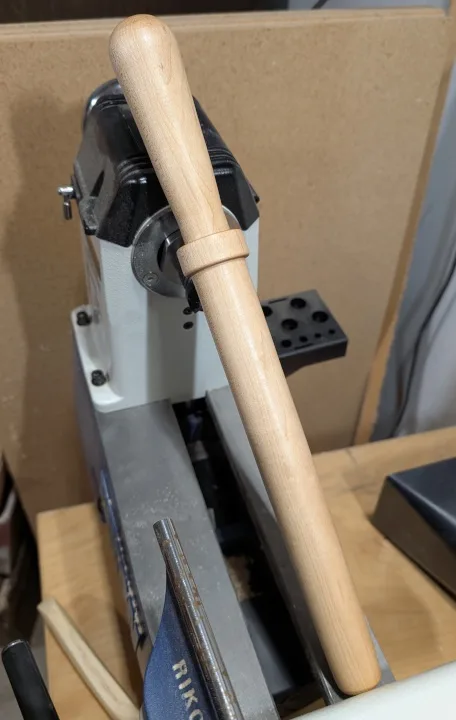 A wooden baseball bat is inserted into a metal machine, likely a lathe or drill press, with the bat's handle resting on the…