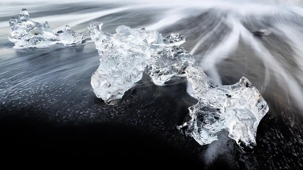 On Iceland's Diamond Beach, glistening ice crystals slowly melt onto dark volcanic sands, surrounded by the Land of Fire and…