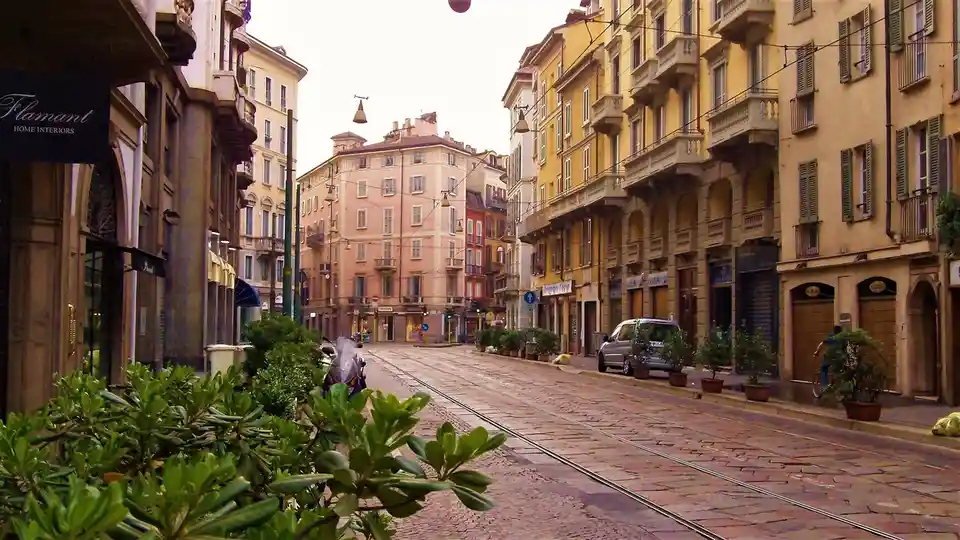 A quiet European street with cobblestone pavement, tram tracks, and colorful buildings, with a person on a bicycle in the…