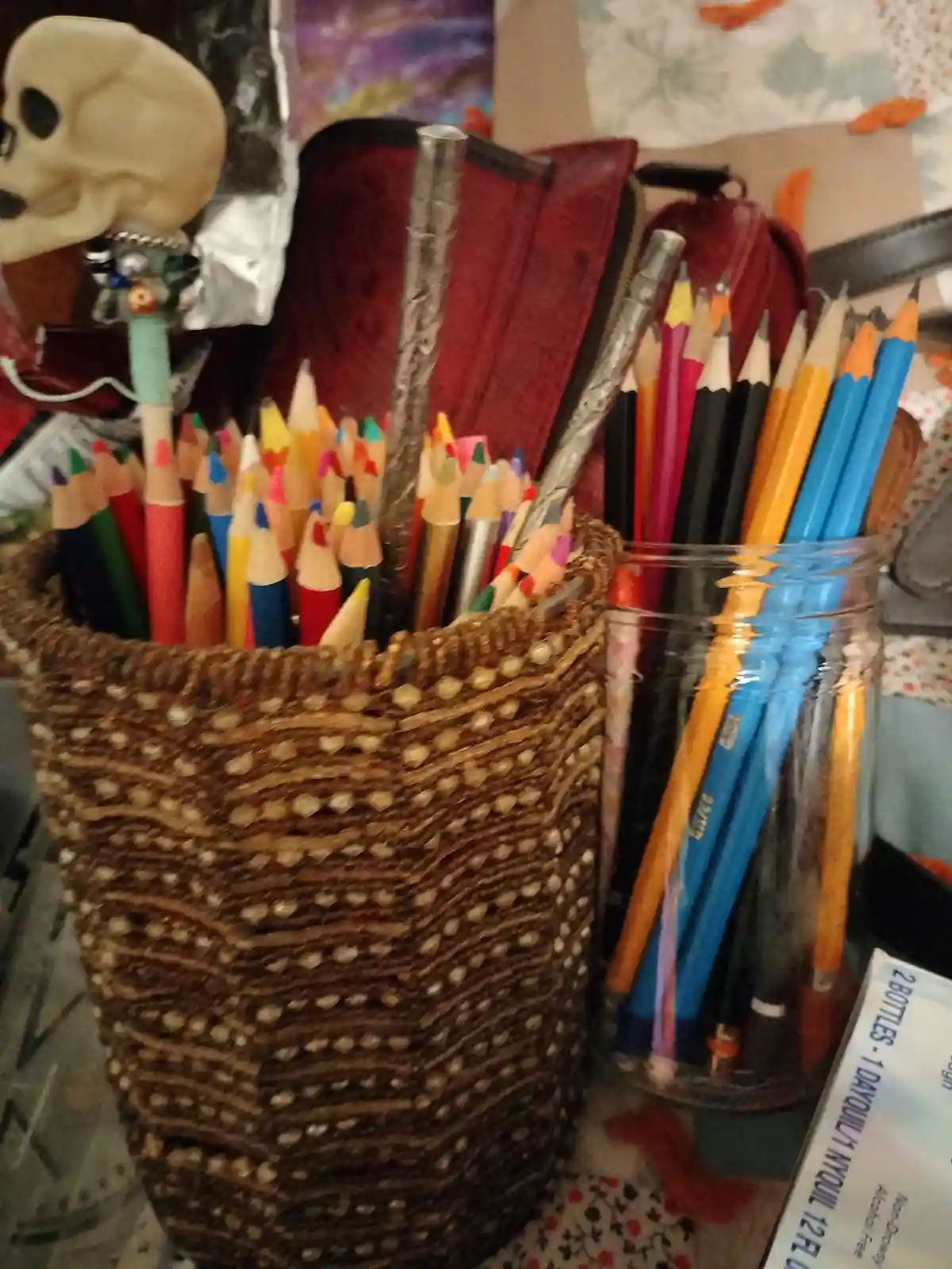 A close-up photo shows two containers overflowing with colorful pencils: a woven basket and a glass jar. A small decorative…