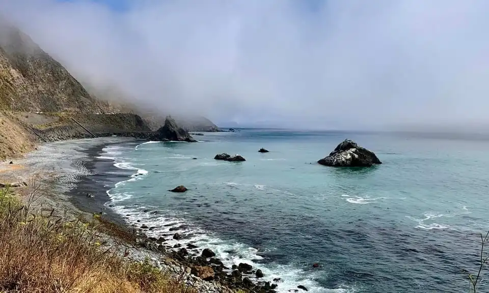 A scenic coastal view with fog rolling over cliffs and waves crashing on a rocky shore, overlaid with the text 'i'm not…