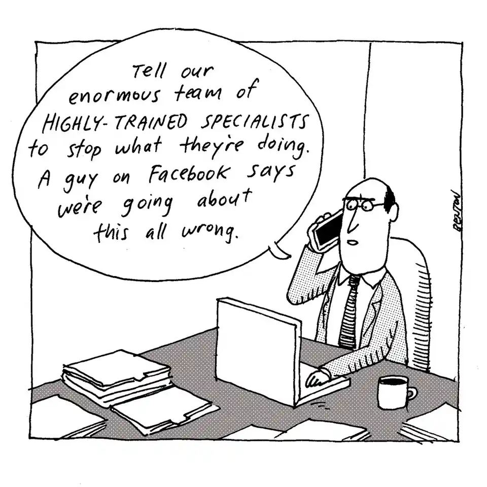 A black-and-white cartoon depicts a man in a suit and tie sitting at a cluttered desk with a laptop, stacks of paper, and a…