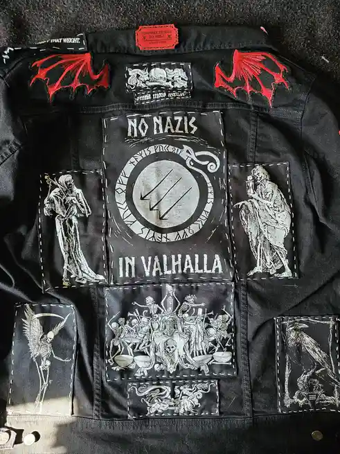 A black denim jacket covered in various embroidered patches, including red bat wings on the shoulders, a central patch…
