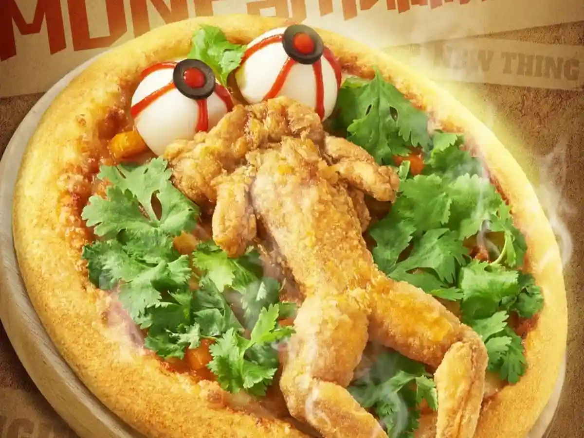 A promotional image of a pizza topped with fried chicken pieces arranged to resemble a humanoid figure, with two hard-boiled…