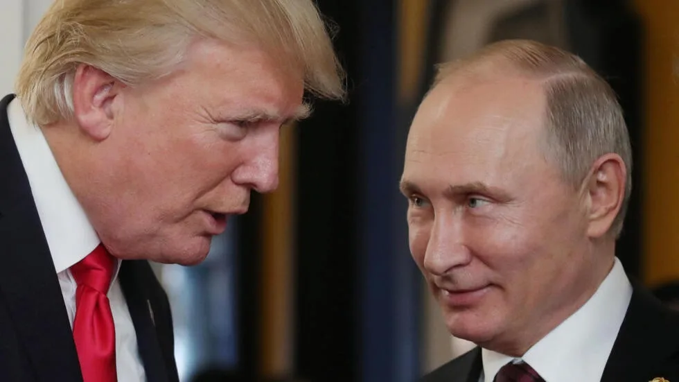 A photo shows Donald Trump leaning in to speak to Vladimir Putin, who looks on with a subtle smirk. Trump wears a red tie…
