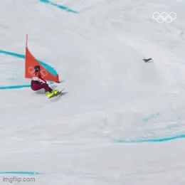 A snowboarder in a red and black outfit navigates a slalom course marked by red flags and blue lines on snow, captured in…
