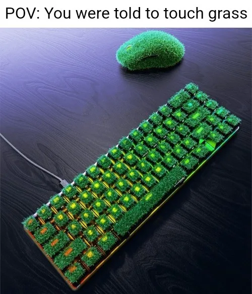 A computer keyboard and mouse are covered in artificial green grass, with glowing green backlighting visible beneath the…