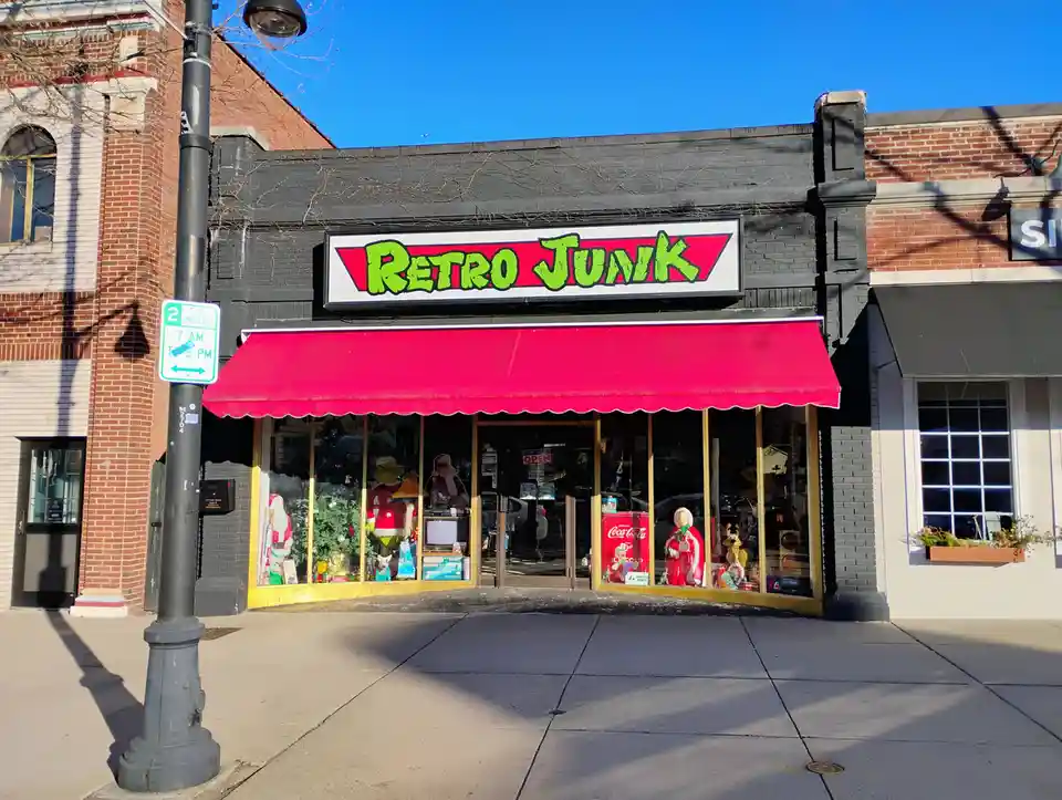 A storefront with a bright red awning and a sign reading 'RETRO JUNK' in green graffiti-style font on a red background. The…