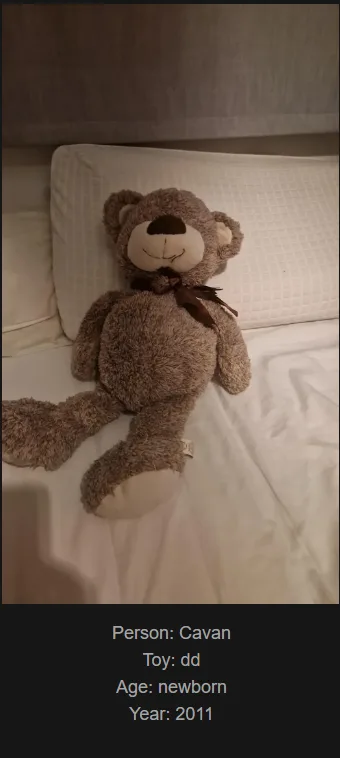 A brown, fluffy teddy bear with a brown bowtie sits upright on a white bed with a textured pillow behind it. The bear has a…