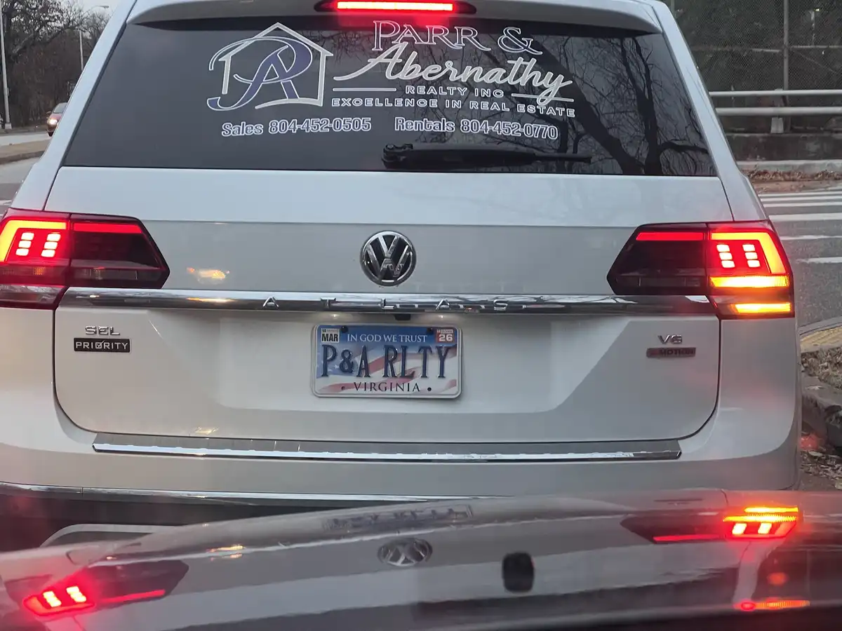 The rear of a white Volkswagen Atlas SUV shows a real estate business decal for 'Parr & Abernathy Realty Inc.' on the back…