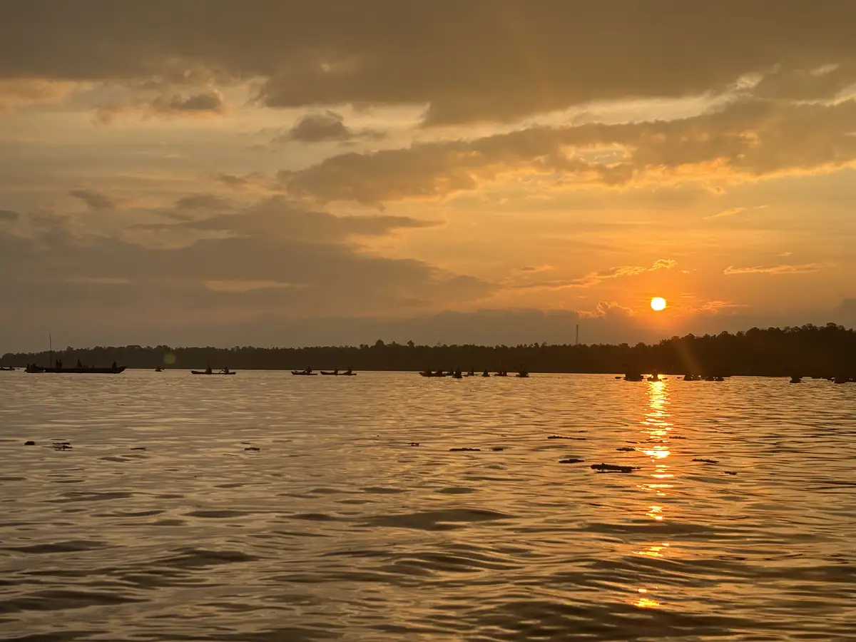 A serene sunset over a calm body of water, with the sun low on the horizon casting golden light and reflections across the…