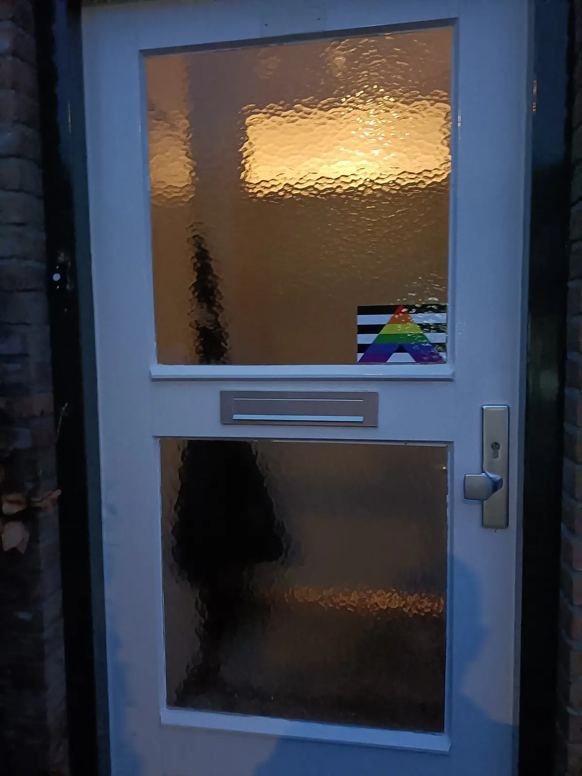 A white front door with textured glass panels, one of which has a small rainbow-colored triangle sticker on it, set against…