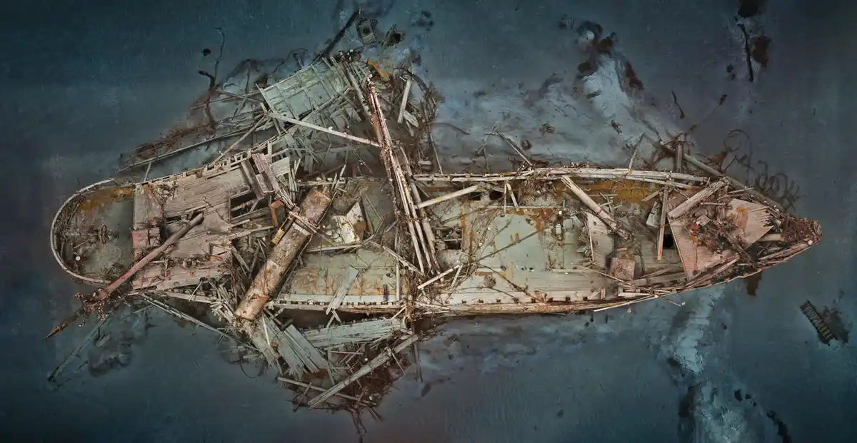 An aerial view shows the skeletal remains of a wooden shipwreck, its broken planks and twisted metal scattered across a…