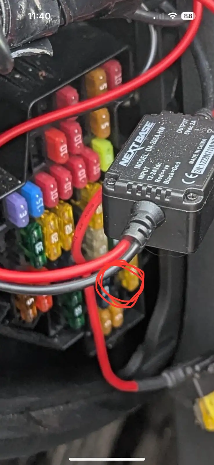 a close-up photo of a car's fuse box with colorful fuses and red wires, where a red circle highlights a fuse that appears…