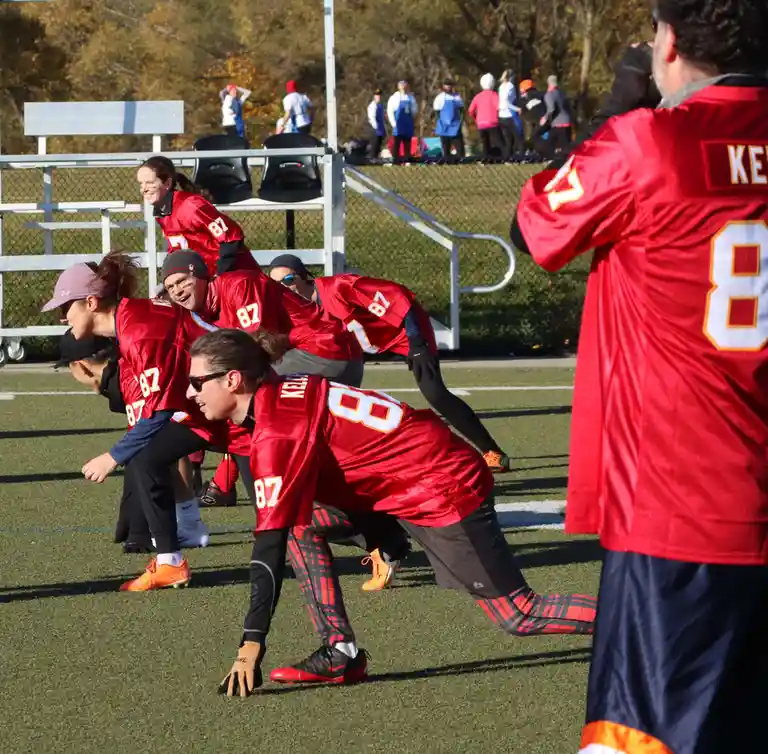 A group of people in red football jerseys are lined up in a huddle on a field, with one person in the foreground wearing…