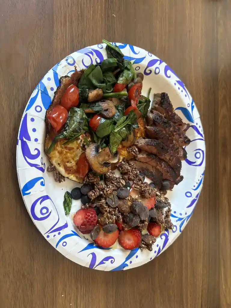 A top-down photo of a plate with a blue and white pattern, holding a breakfast meal that includes sliced steak, a fried egg…