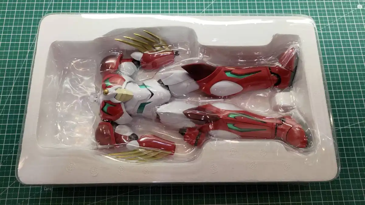 A red and white robot action figure is shown lying on its back inside its clear plastic packaging, which is nestled in a…