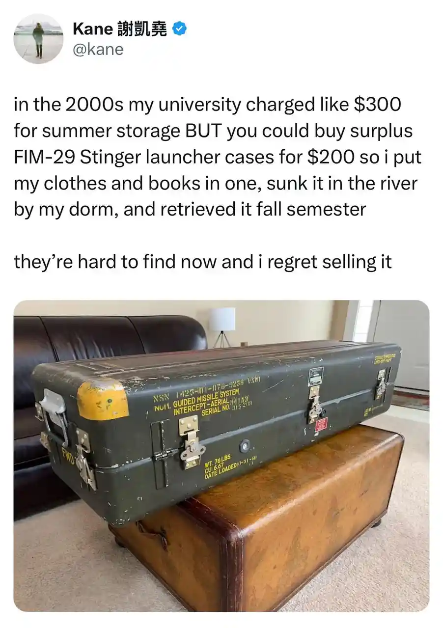 A large, olive-green military-style case labeled 'FIM-29 Stinger' sits on top of a brown leather suitcase in a living room…