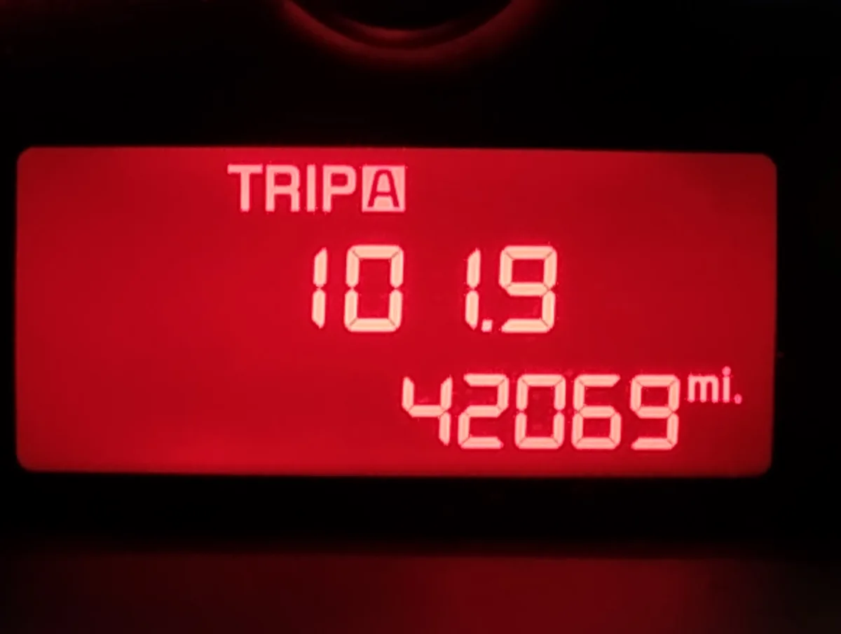 A red digital car odometer display shows 'TRIPA' at the top, followed by '10 1.9' and '42069 mi.' below. The numbers are in…