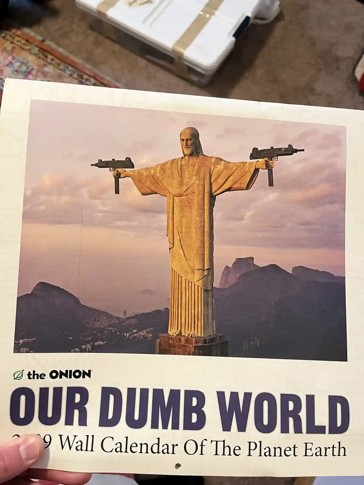 A person holds up a 2009 'Our Dumb World' wall calendar from The Onion, which features a digitally altered image of the…