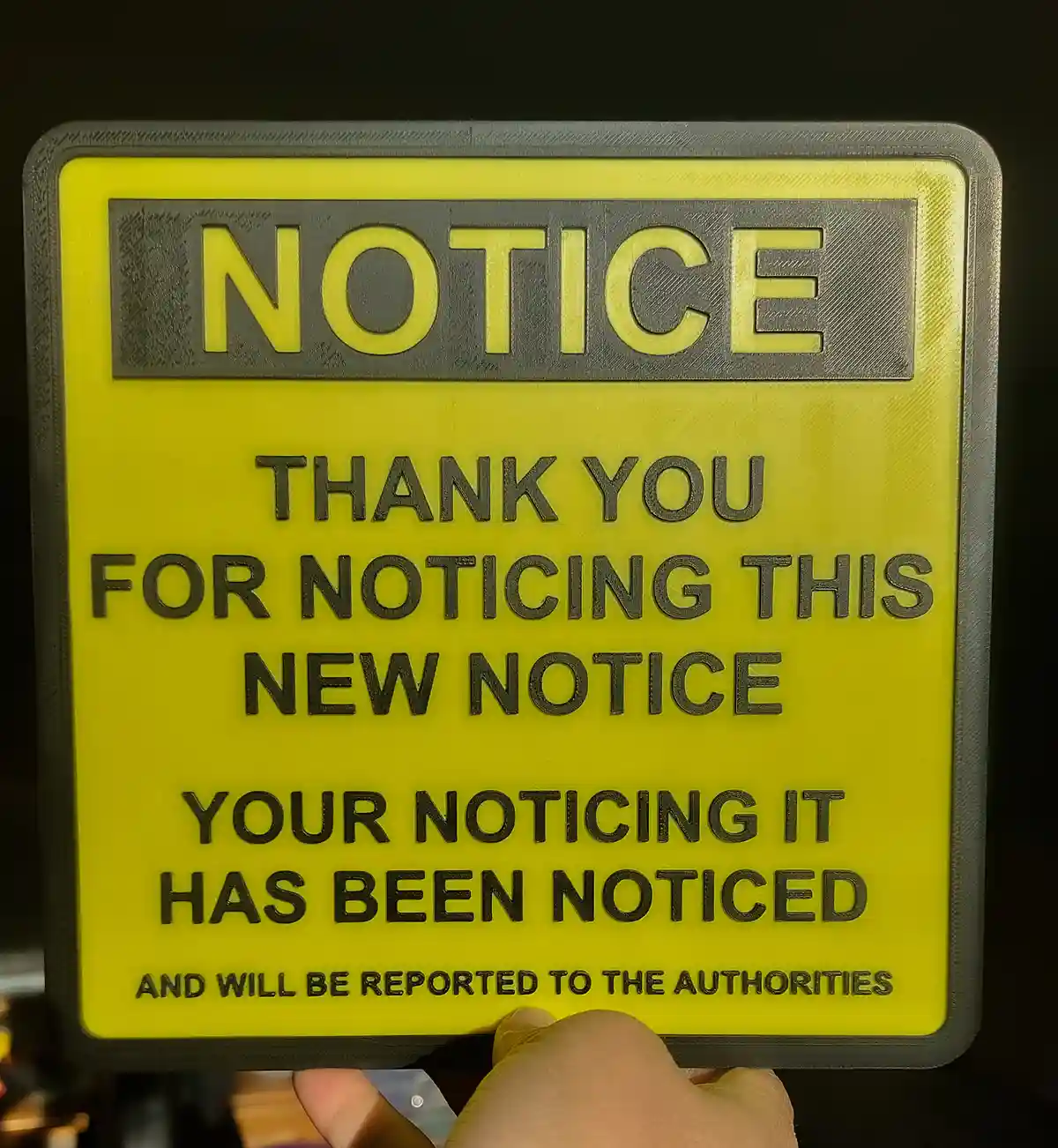 A bright yellow 3D-printed sign with a black border and raised text reads 'NOTICE' at the top, followed by 'THANK YOU FOR…