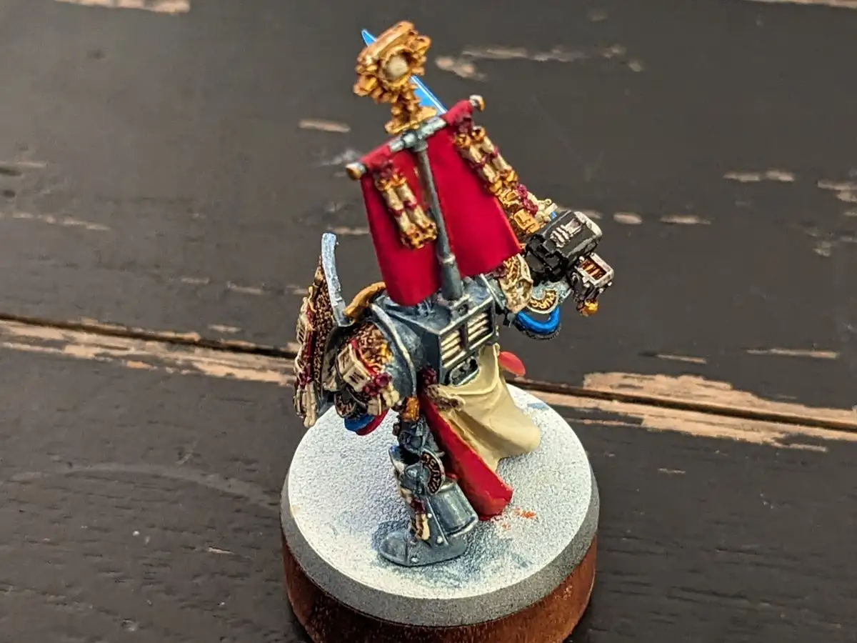 A highly detailed, hand-painted miniature of a space marine stands on a circular base, holding a red banner and a weapon…