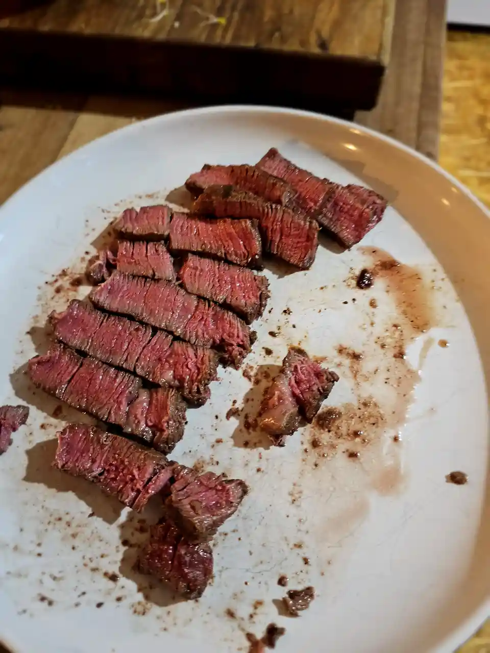 A white plate holds sliced, medium-rare steak with visible juices and charred edges, set on a wooden surface. The overlaid…