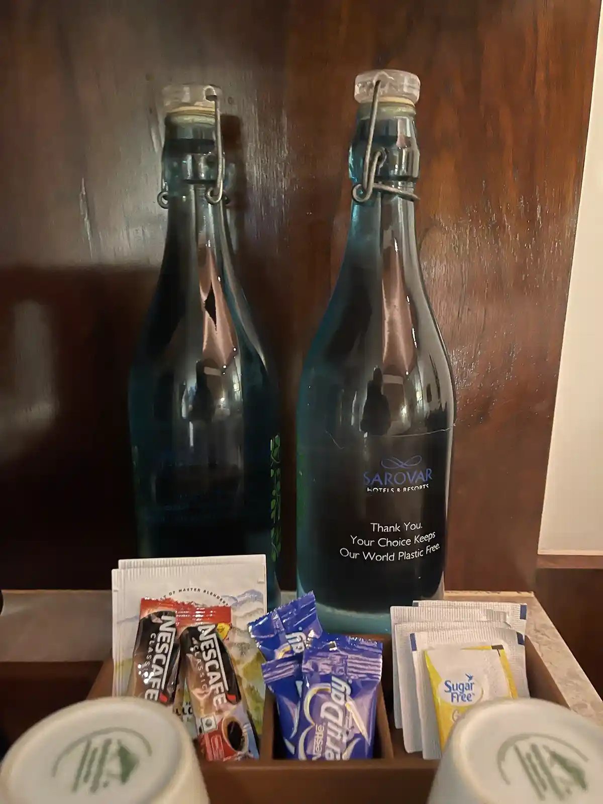 Two blue glass bottles with swing-top lids sit on a wooden surface, one labeled 'SAROVAR HOTELS & RESORTS' with the text…