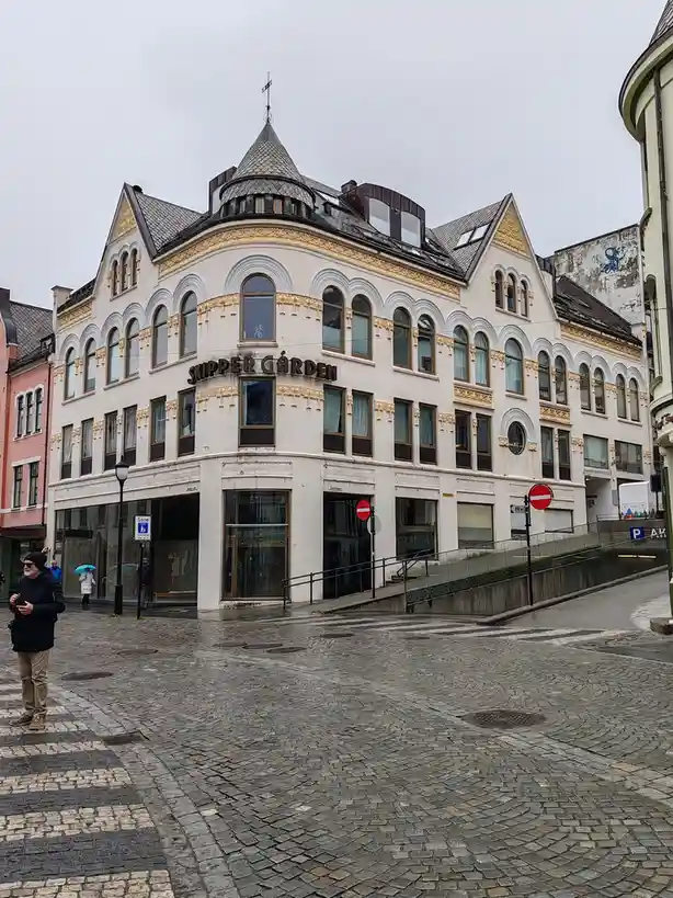 A photo of a white, ornate, corner building with arched windows and gold trim, labeled 'SKIPPER GÅRDEN' on its facade, set…