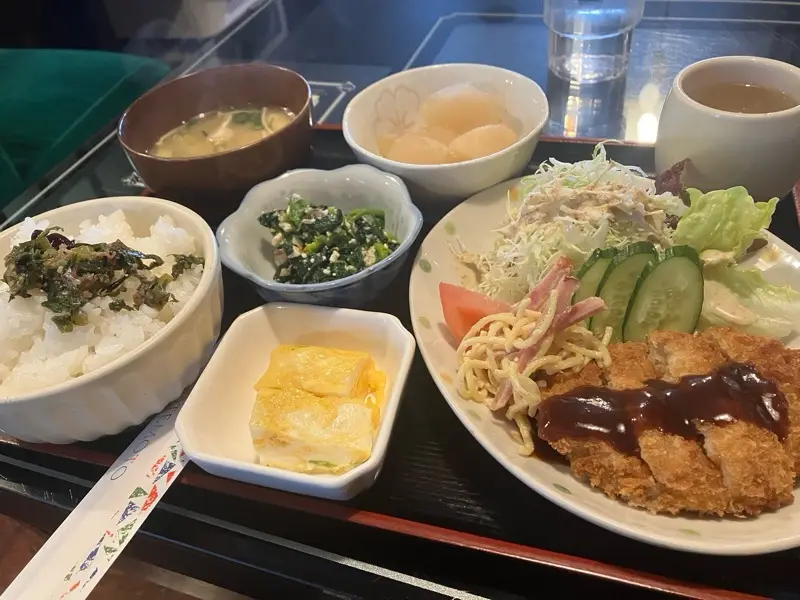 a full japanese meal is laid out on a black tray with red trim, featuring a large plate of fried chicken with sauce, a side…