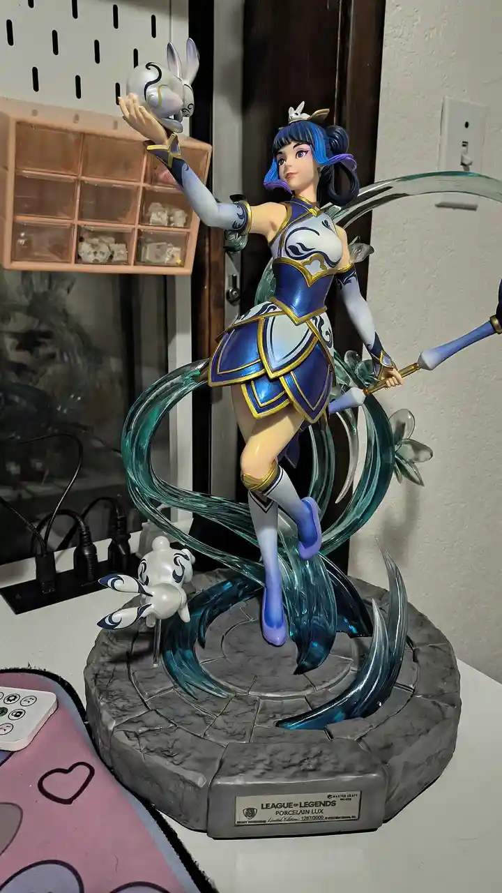 A detailed figurine of Lux from League of Legends, dressed in a blue and white porcelain-themed outfit with gold trim…