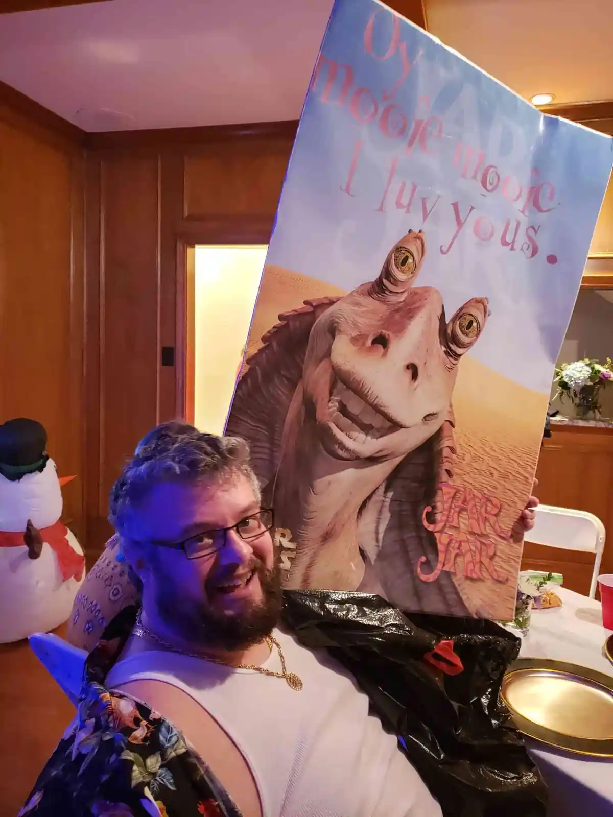 A smiling man with glasses and a beard holds up a large poster of the Star Wars character Jar Jar Binks, which has been…