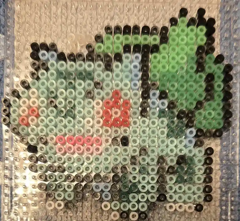 An overhead shot of a pixel art piece made from small, round, colored beads arranged on bubble wrap. The beads form a…