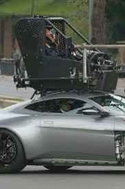 a silver sports car has a black helicopter mounted on its roof, with a person visible inside the helicopter's cockpit. the…
